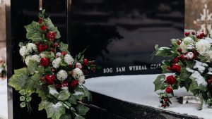Snow-covered tombstone with red roses and white flowers, symbolizing winter's serene beauty in a cemetery.