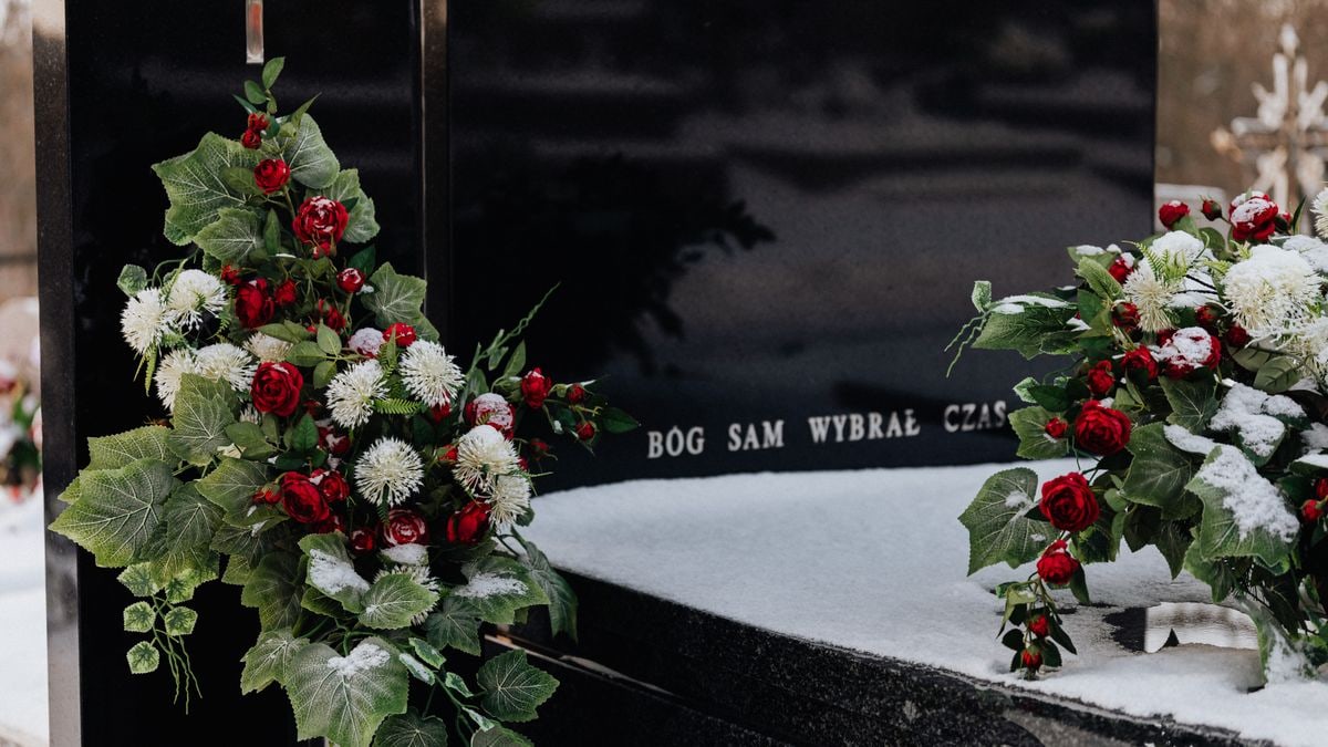 Snow-covered tombstone with red roses and white flowers, symbolizing winter's serene beauty in a cemetery.