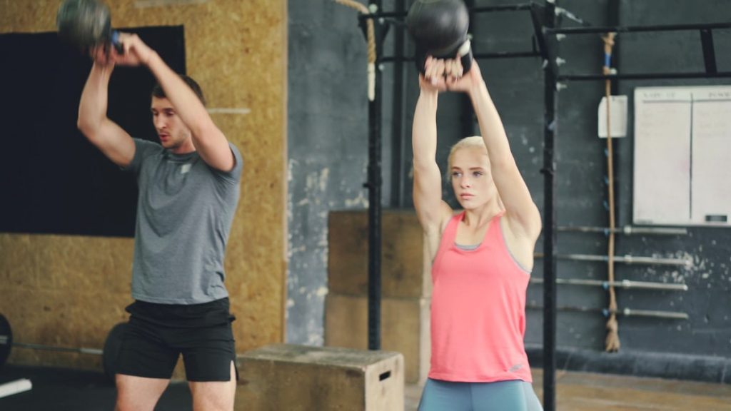 Young woman and man are working out with heavy dumbbells squatting and lifting weight exercising indoors in modern sports gym. People and lifestyle concept.