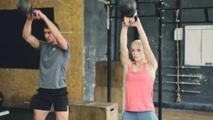 Young woman and man are working out with heavy dumbbells squatting and lifting weight exercising indoors in modern sports gym. People and lifestyle concept.