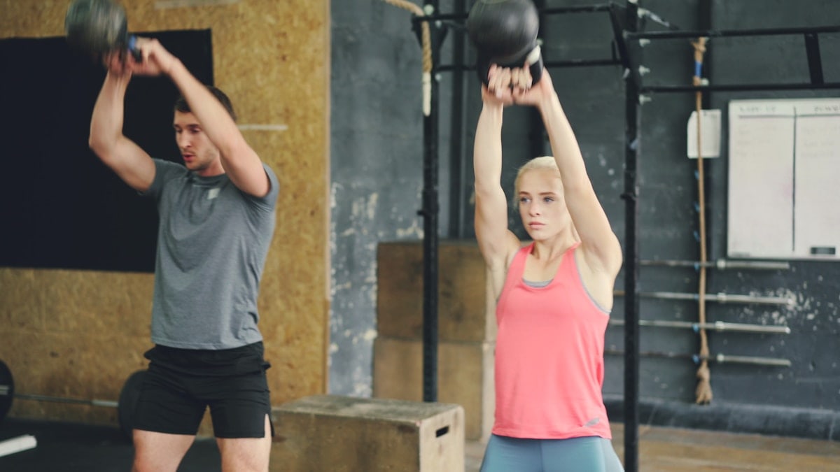 Young woman and man are working out with heavy dumbbells squatting and lifting weight exercising indoors in modern sports gym. People and lifestyle concept.